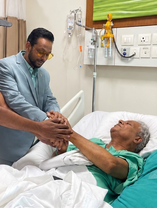 An OMCA Foundation volunteer holding the hand of a patient in a hospital bed